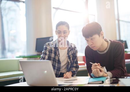 Two students sitting at the table and using laptop computer in their study in the classroom Stock Photo