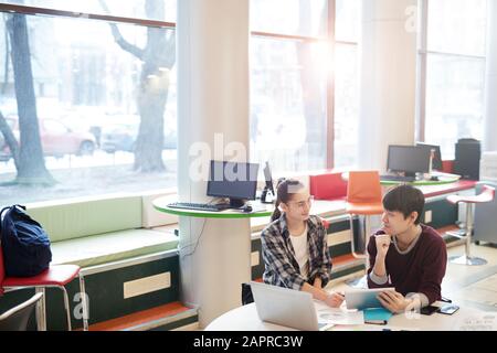 Two college students sitting at desk in front of laptop computer and using digital tablet they working online in team Stock Photo