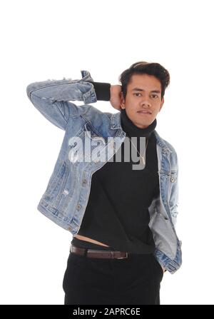 A close up image of a young tall man with one hand behind his head, in a jeans jacket and black sweater, isolated for white background Stock Photo