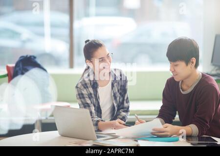 Two college students sitting at the table with laptop computer and discussing report together in the classroom Stock Photo