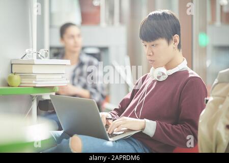 Asian serious man sitting on sofa and typing on laptop computer he concentrating on his online work Stock Photo