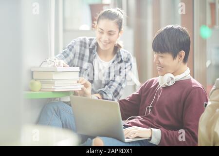 Asian young man sitting and using laptop with young woman who bringing the books and helping him in study Stock Photo