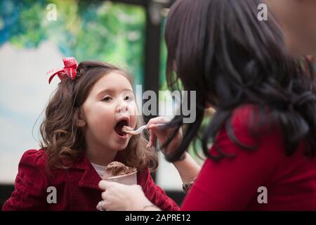 Mother feeding ice cream to young daughter Stock Photo