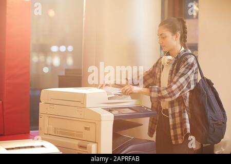 College student with backpack using printer to make the copy of report at university Stock Photo