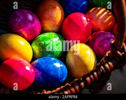 Close-up of Easter eggs in various colors collected in wicker basket on sunny April morning (springtime). Egg hunt German Easter holiday tradition. Stock Photo