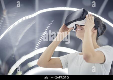 Young woman wearing virtual glasses smiling while playing in virtual video game Stock Photo