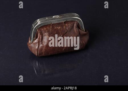 A closed brown used leather purse reflected on dark background. Stock Photo