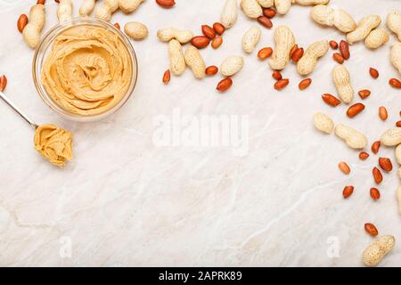 Peanut butter in glass plate with peanuts in shell, peeled peanuts, spoon with peanut butter. Creamy peanut paste flat lay with place for text on Stock Photo