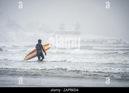 Surfer walking out to waves during a snow storm in Maine Stock Photo