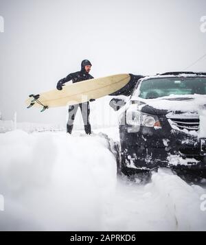 Surfer putting surfboard on top of car during winter snow storm Stock Photo