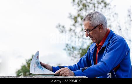 Old man with glasses reading the newspaper at park with the sky and the tree in the background Stock Photo