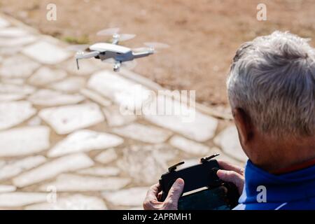 Rear view of the elderly man piloting the drone looking at the remote control display while standing, selective focus Stock Photo