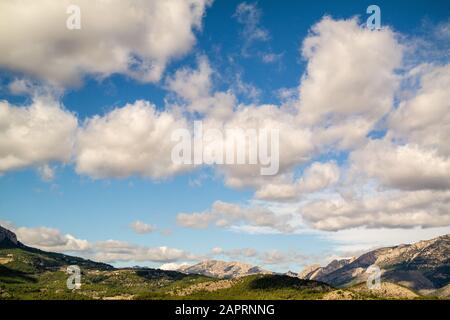 Beautiful shot of a blue sky full of clouds above mountains covered in trees in Polop, Spain Stock Photo