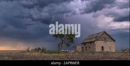 A forked lightning bolt descends from a weak thunderstorm near an abandoned building; Guymon, Oklahoma, United States of America Stock Photo
