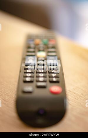 Vertical closeup shot of a remote controller on a wooden surface with a blurred background Stock Photo