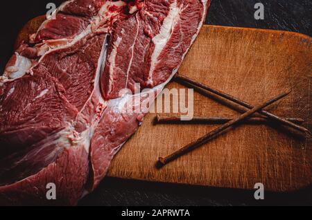 Raw beef rusty nails on a cutting board. Fresh meat and three old nails on a dark background. Ambiguous meaning. Selective focus. Without people. Stock Photo