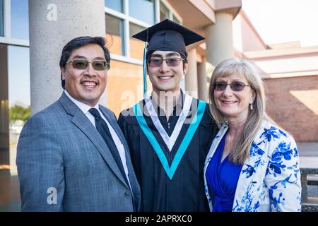 A young man wearing a cap and gown stands with his parents for a portrait on graduation day; Surrey, British Columbia, Canada Stock Photo