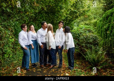 Family portrait of parents kissing and kids watching while all standing on a trail in a forest; Langley, British Columbia, Canada Stock Photo