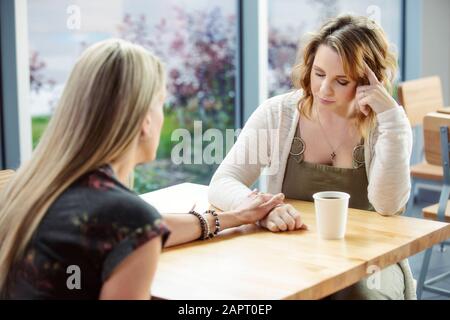 A mature Christian woman mentoring and praying with a young woman during a bible study in a coffee shop at a church: Edmonton, Alberta, Canada Stock Photo