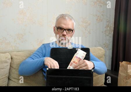 A business man puts money into a black leather briefcase. Business Stock Photo