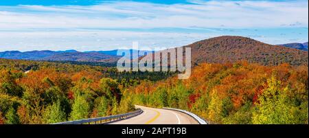 Autumn coloured foliage in a forest over the hills and a road running through it in the Laurentian Mountains; Mont-Tremblant, Quebec, Canada Stock Photo