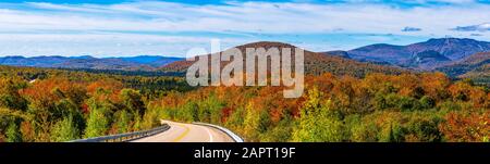 Autumn coloured foliage in a forest over the hills and a road running through it in the Laurentian Mountains; Mont-Tremblant, Quebec, Canada Stock Photo