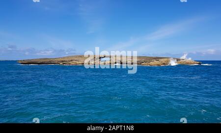 A wave breaks on small island off the coast of Oahu, Hawaii shoots water high into the air. Stock Photo