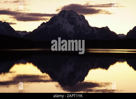 The still lake perfectly reflects the mountain in the background in the waning light after sunset. Stock Photo