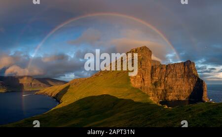 A full rainbow at sunset over the cliffs of the island of Vagar. Faroe Islands Stock Photo