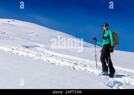Woman backcountry skiing, climbing up mountain in skin track, on AT skis and skins in Hatcher's Pass, Alaska, Talkeetna Mountains Stock Photo