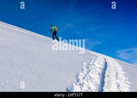 Woman backcountry skiing, climbing up mountain in skin track, on AT skis and skins in Hatcher's Pass, Alaska, Talkeetna Mountains Stock Photo