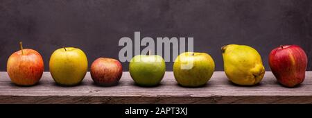 on the rough wooden table, seven apples of different types Stock Photo
