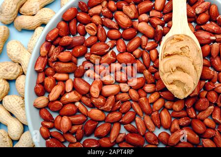 Creamy peanut paste in wooden spoon on peanuts. Near the peanut butter lies peanuts in the shell and peeled peanuts. Minimalistic food flat lay on Stock Photo