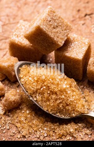 In the foreground, raw cane sugar crystals in the spoon. In the background some sugar cubes Stock Photo