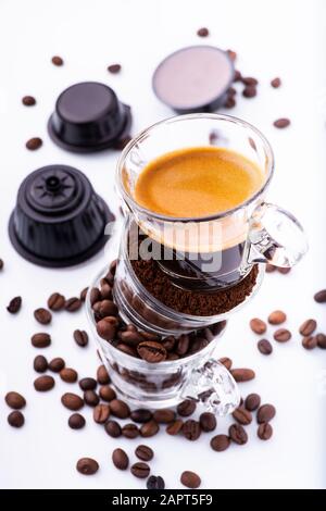 glass cups, in vertical sequence, with coffee beans, ground, and creamy espresso. In the background some coffee capsules Stock Photo