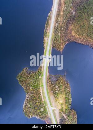 Beautiful view from a road going through the beautiful lake and forest, surrounded with water on both sides, shot above from drone, aerial vibrant pic Stock Photo