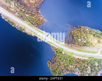 Beautiful view from a road going through the beautiful lake and forest, surrounded with water on both sides, shot above from drone, aerial vibrant pic Stock Photo