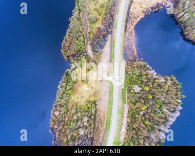 Beautiful view from a road going through the beautiful lake and forest, surrounded with water on both sides, shot above from drone, aerial vibrant pic Stock Photo