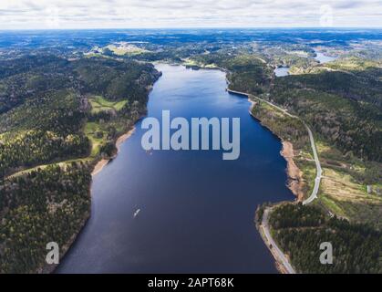 Beautiful view from a road going through the beautiful lake and forest, surrounded with water on both sides, shot above from drone, aerial vibrant pic Stock Photo