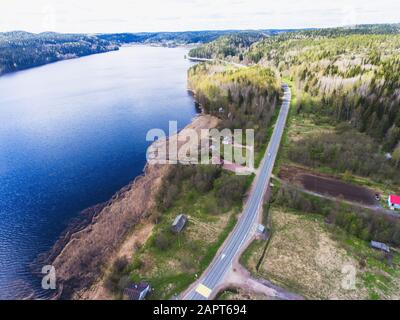 Beautiful view from a road going through the beautiful lake and forest, surrounded with water on both sides, shot above from drone, aerial vibrant pic Stock Photo