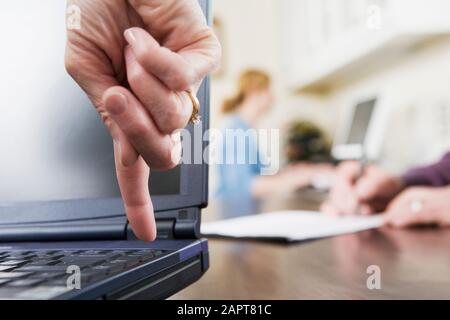 A woman's finger pointing downwards towards a key on a laptop keyboard