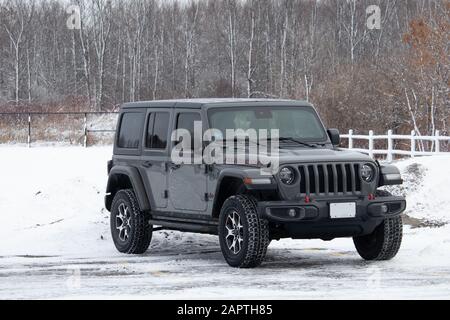 A late model Jeep Wrangler JL Unlimited Rubicon 4x4 SUV, first seen in the 2018 model year, is parked in a snowy parking lot before trees in winter. Stock Photo