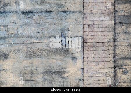 A section of an old concrete wall with a vertical column of bricks shows a variety of textures and lines where it has been patched and repaired. Stock Photo