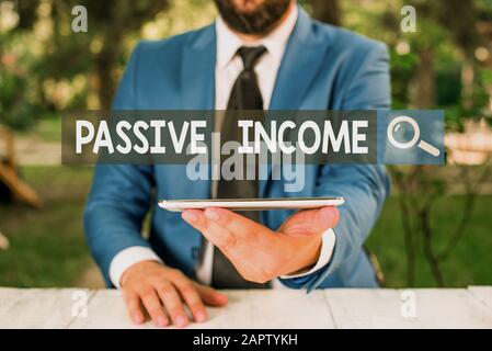 Text sign showing Passive Income. Business photo showcasing the earnings derived from a rental property and others Businessman with mobile phone in hi Stock Photo