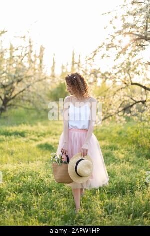 Young attractive woman with curly hair walking in a green flowered garden. Spring romantic mood. Stock Photo