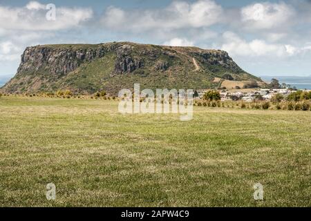 Stanley, Tasmania, Australia - December 15, 2009: The Nut volcanic plug and part of town behind hay field under dark cloudscape. Stock Photo