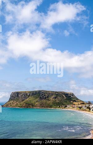 Stanley, Tasmania, Australia - December 15, 2009: Portrait of The Nut volcanic plug under blue cloudscape.  Blue ocean in front and some white houses Stock Photo