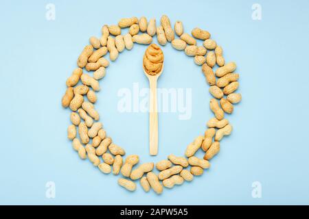 Creamy peanut paste in wooden spoon. Peanuts in the peel scattered on blue background. Minimalistic food flat lay on color blue background. Stock Photo