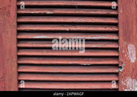 Close up of a dirty old red wooden window shutter with weathered and cracked paint peeling off Stock Photo