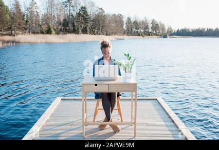 woman flexible working on a desk on a pier at the beach Stock Photo